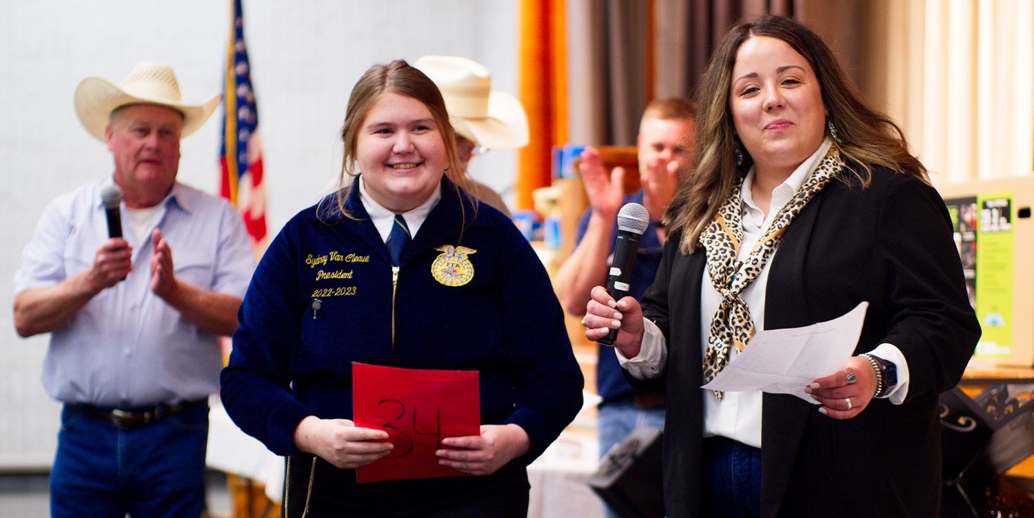 Sydney van Cleave holds a card representing the 34th hay bale auctioned off for the evening as emcee Jackie Rodieck prepares to make some remarks. [we have more hay moments here]